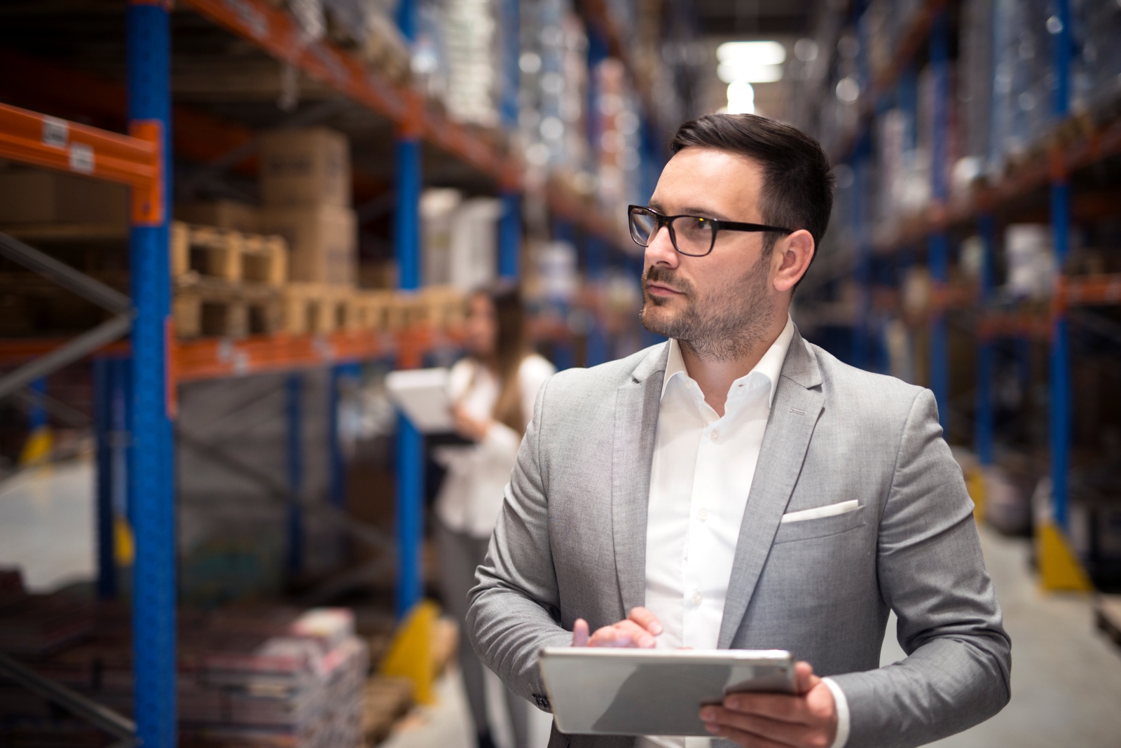 portrait successful businessman manager ceo holding tablet walking through warehouse storage area looking towards shelves | Logistics and Supply Chain Courses